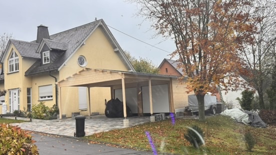 Finales Bild des fertig montierten Carports in Holzbauweise am gelben Wohnhaus, nach Abschluss der Montage