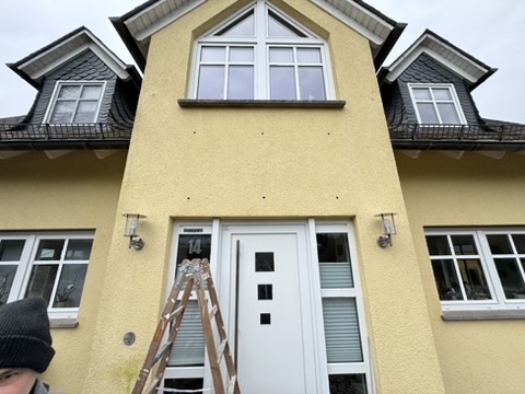 Hauseingang vor der Vordachmontage: gelbe Fassade, weiße Haustür und bereitgestellte Leiter