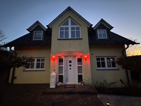 Fertig montiertes transparentes Vordach über der Haustür, aufgenommen am Abend mit eingeschalteter Eingangsbeleuchtung